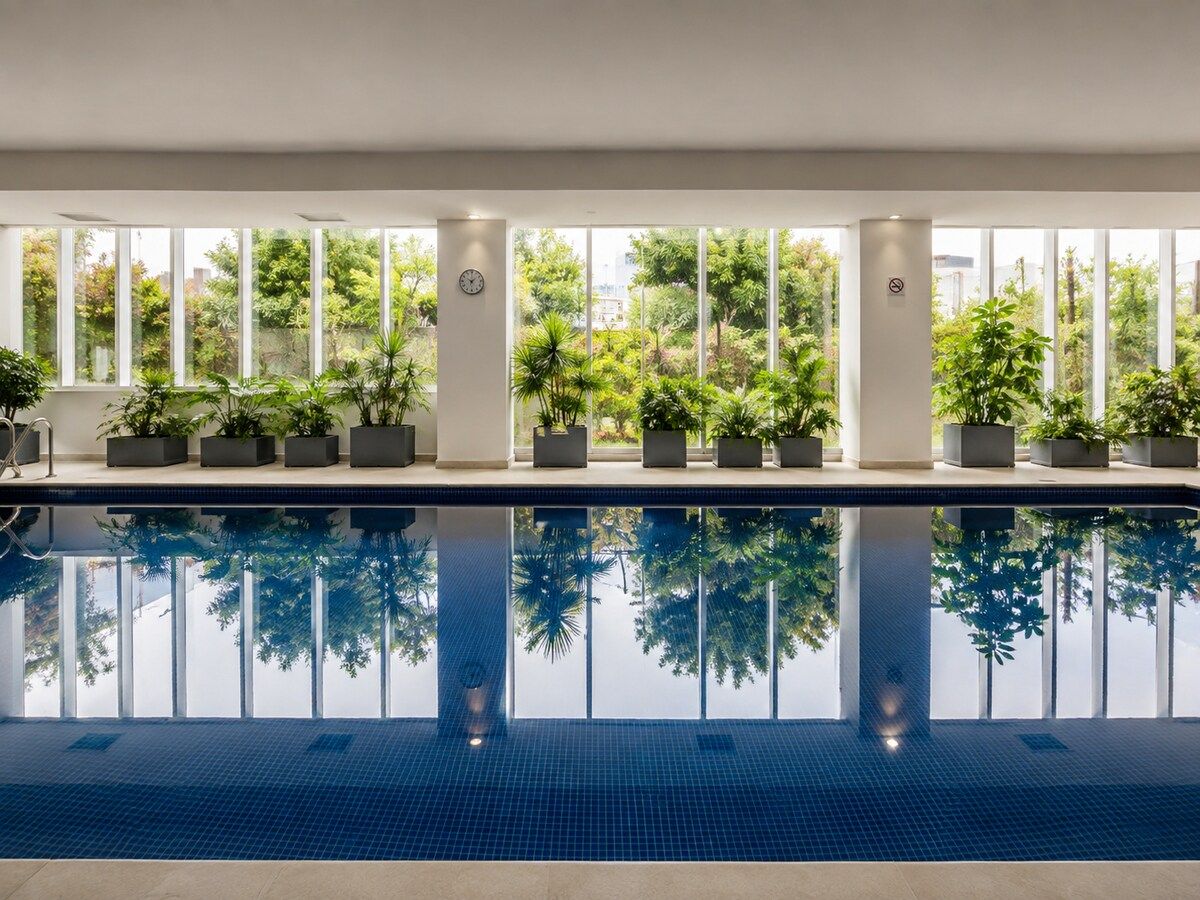 Une piscine intérieure aux eaux cristallines, entourée de fenêtres et agrémentée de plantes en pot.