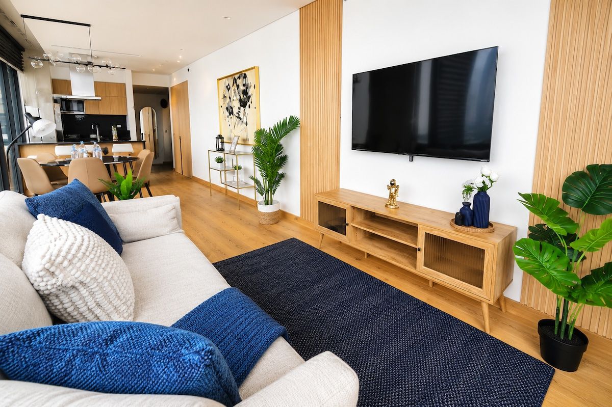 Ein modernes Wohnzimmer mit einer Couch, einem Fernseher, einer Holz-Unterhaltungseinrichtung und einem Essbereich im Hintergrund.
