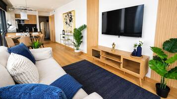 Ein modernes Wohnzimmer mit einer Couch, einem Fernseher, einer Holz-Unterhaltungseinrichtung und einem Essbereich im Hintergrund.