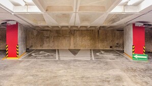 Garagem subterrânea com pilares de concreto, vagas demarcadas e placa de rota de fuga.