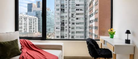 Ein modernes Apartment mit großem Fenster, einer Couch, einem Schreibtisch und einem Sessel.