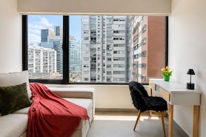 Een modern appartement met een groot raam, een bank, een bureau en een stoel.