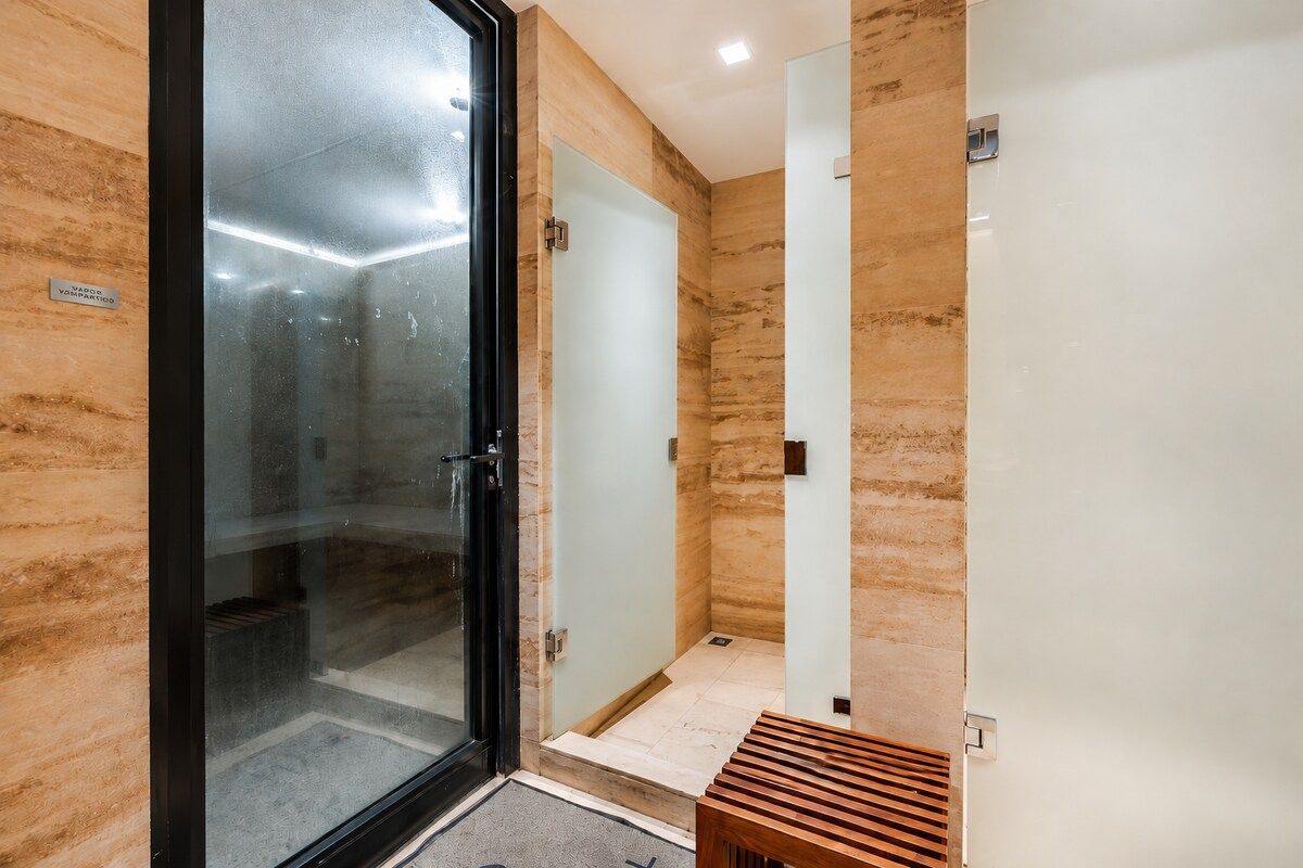 A modern bathroom with a glass shower enclosure, a wooden bench, and a marble wall.
