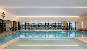Piscina interior moderna com paredes de vidro transparente, chão ladrilhado e um símbolo de cruz na parede.