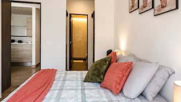 Quarto com cama, almofadas, cobertor, mesa de cabeceira e planta na parede.