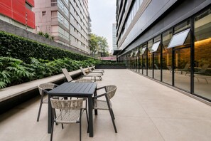 An outdoor seating area with tables and chairs, surrounded by greenery and modern buildings. - Luxury 1BR Condo w/ Pool, Jacuzzi, Near Antara (Mexico City)