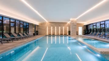 An indoor swimming pool with lounge chairs and a stone wall.