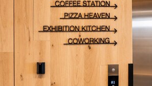 Paret de fusta amb indicadors direccionals que mostren diferents serveis com a saló privat, restaurant, espai per al cafè, cel de pizza, cuina d'exhibició i espai de coworking.