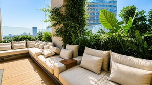 A rooftop terrace with a long sofa, cushions, and a wooden table. - 24th Floor CDMX Condo: Pool, Gym, Panoramic Views (Mexico City)