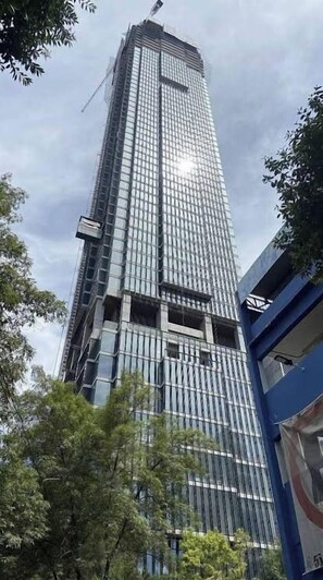 A tall, modern building with a glass facade, surrounded by trees and a blue structure. - 24th Floor CDMX Condo: Pool, Gym, Panoramic Views (Mexico City)
