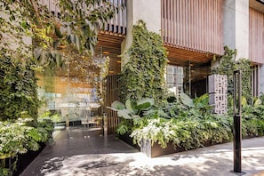 A modern building with a glass facade, vertical garden, and a pathway leading to the entrance. - 24th Floor CDMX Condo: Pool, Gym, Panoramic Views (Mexico City)
