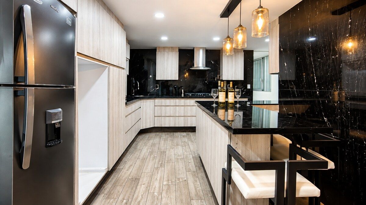 A modern kitchen with a built-in refrigerator, wooden cabinets, a black countertop, and pendant lighting.