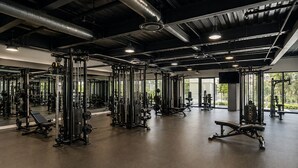 Kuntosali, jossa on monenlaisia kuntoilulaitteita, suuret ikkunat ja korkea katto.