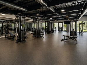 Ein Fitnessstudio mit unterschiedlichen Trainingsgeräten, großen Fenstern und einer hohen Decke.