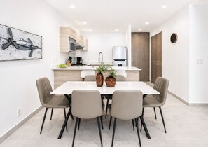 A modern kitchen with a dining area, featuring a white countertop, a stainless steel refrigerator, and a dining table with four chairs. - Polanco Condo: Heated Pool, Gym & Antara Access (Mexico City)
