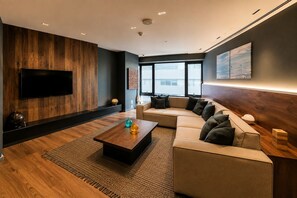 Una sala de estar moderna con un televisor de pantalla plana, un sofá modular, una mesa de centro y un ventanal grande.