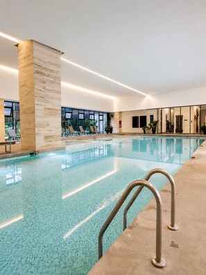 Une piscine intérieure à l’eau claire, avec un sol carrelé et quelques chaises longues.