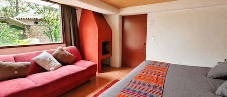 Una habitación con un sofá rojo, una cama con una colcha a rayas y una ventana con vistas a zonas verdes.