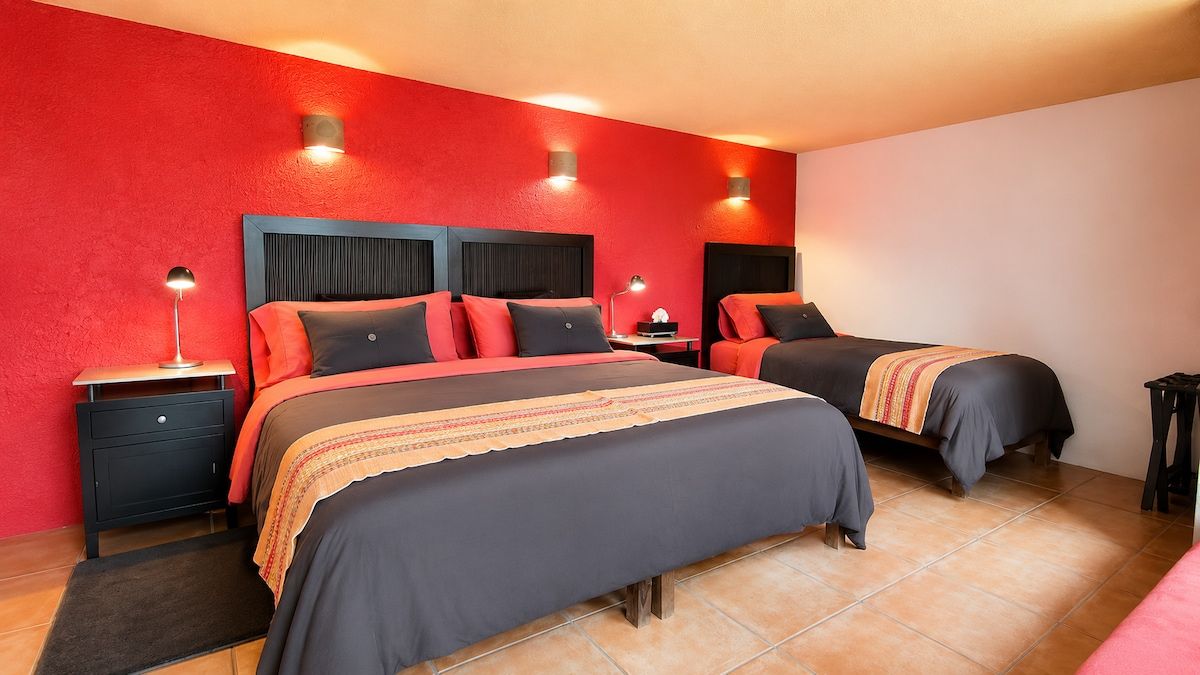 A hotel room with two beds, a red accent wall, and a tiled floor.