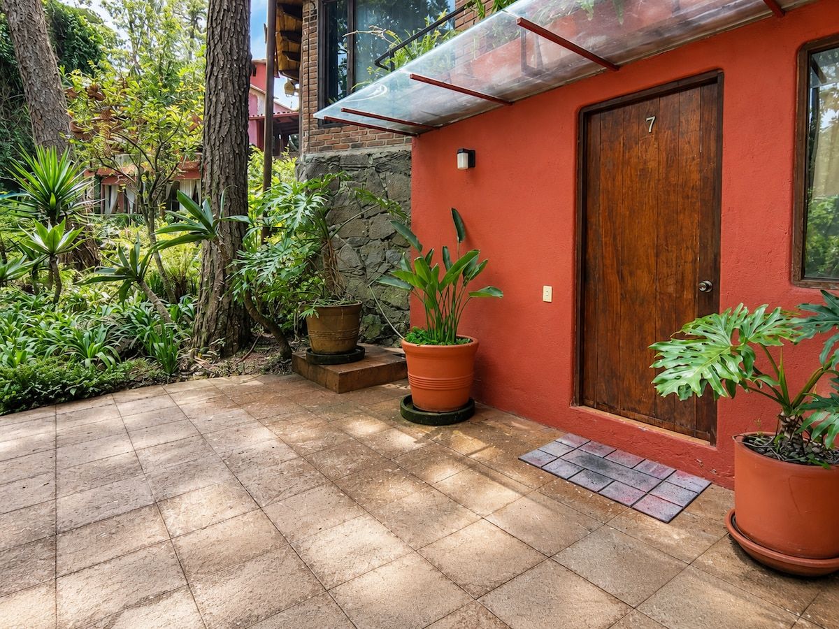 A red building with a wooden door, potted plants, and a tiled patio.