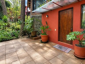 A red building with a wooden door, potted plants, and a tiled patio.