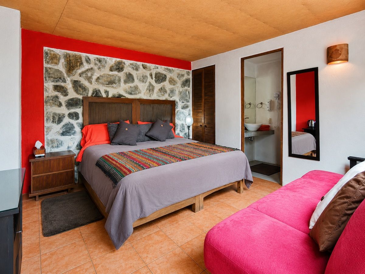 A bedroom with a stone wall, a bed with a colorful blanket, a wooden headboard, and a red accent wall.