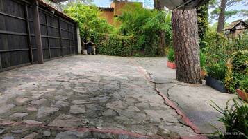 A courtyard with a stone floor, a wooden gate, and a tree.