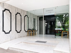 Entrada de hotel com parede de mármore, porta de vidro e balcão de recepção.
