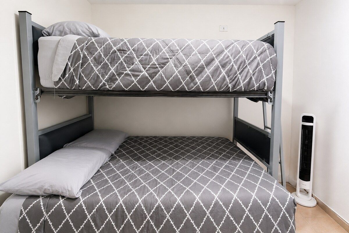 Uma cama beliche com colcha estampada, um travesseiro e um aquecedor portátil.
