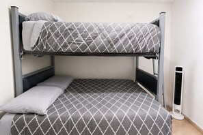 Uma cama beliche com colcha estampada, um travesseiro e um aquecedor portátil.