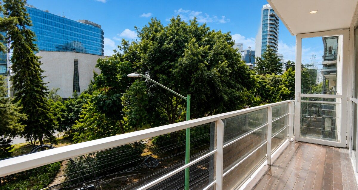 Uma varanda com vista para paisagem urbana, incluindo um edifício moderno e árvores.
