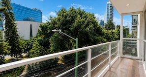 Uma varanda com vista para paisagem urbana, incluindo um edifício moderno e árvores.