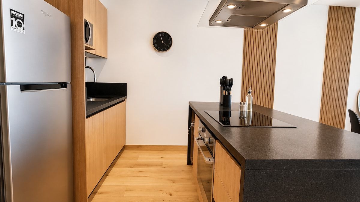 Una cocina compacta con refrigerador, microondas y un reloj en la pared.