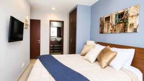 Ein Schlafzimmer mit einem Bett, Kissen, einem Fernseher, einem Kleiderschrank und einem durch eine offene Tür einsehbaren Badezimmer.