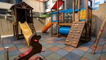 Uma área de recreação infantil com escorrega, estrutura de escalada e casinha de madeira.