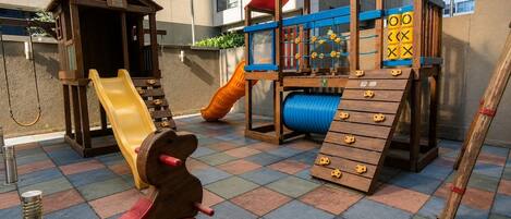 Un espace de jeux pour enfants avec un toboggan, une structure d’escalade et une maison de jeu en bois.