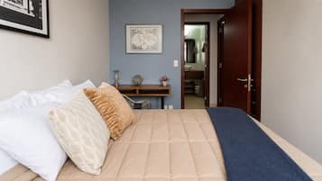 Um quarto com cama, escrivaninha e porta para um banheiro.