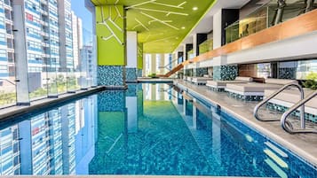 Piscina interior moderna com paredes de vidro transparente, piso revestido e escada que leva aos andares superiores.