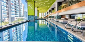A modern indoor swimming pool with clear glass walls, a tiled floor, and a staircase leading to upper levels. - Polanco 20th-Floor Condo: Pool, Gym, City Views (Mexico City)