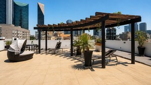 A rooftop terrace with outdoor seating, potted plants, and a city skyline in the background. - Condesa Loft w/ Pool, Sauna & Private Parking (Mexico City)