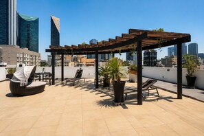 Une terrasse sur le toit, avec des sièges en plein air, des plantes en pot et une vue panoramique sur la ville en arrière-plan.