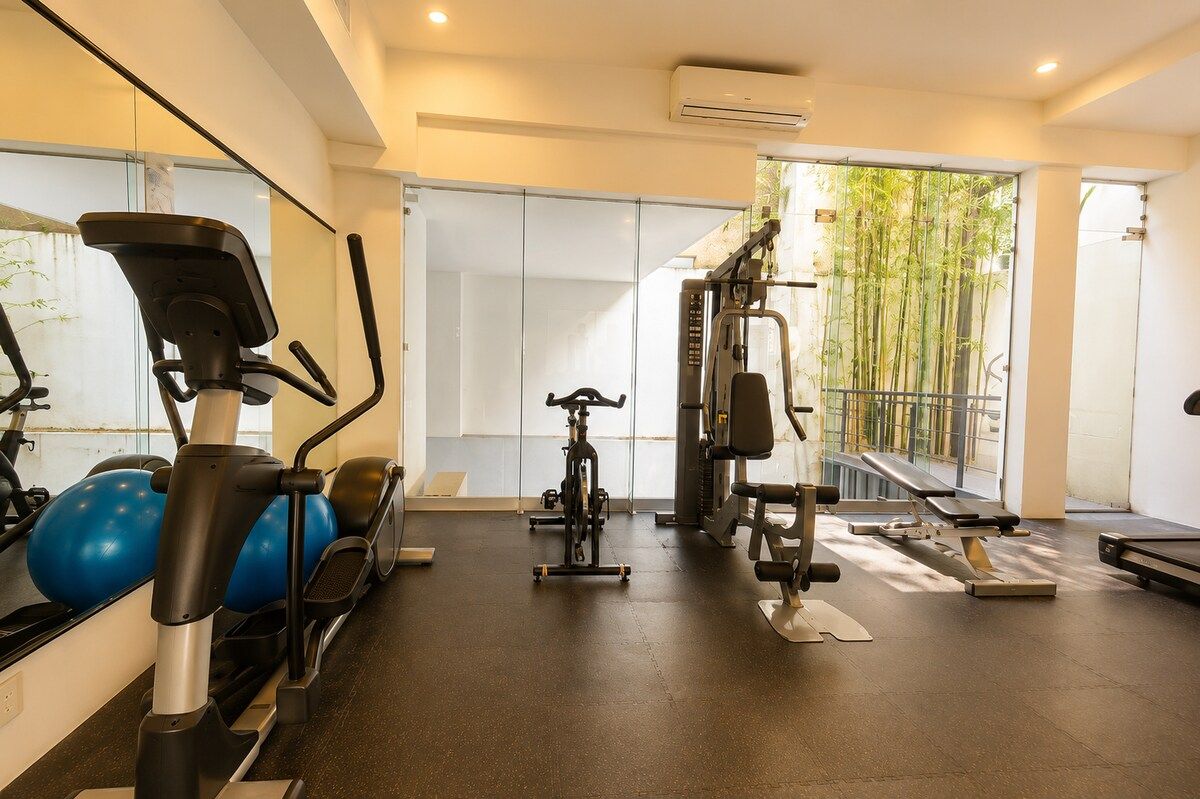 A gym with cardio machines, weightlifting equipment, and a large window with a view of bamboo outside. - Condesa Loft w/ Pool, Sauna & Private Parking (Mexico City)