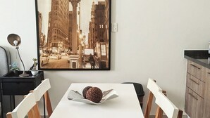 A dining area with a white table and wooden chairs, a framed cityscape picture on the wall, and a small potted plant on the side table. - Condesa Loft w/ Pool, Sauna & Private Parking (Mexico City)