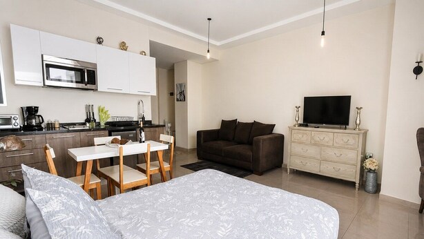 A modern living space with a large bed, a dining area, a sofa, a TV, and a kitchen area. - Condesa Loft w/ Pool, Sauna & Private Parking (Mexico City)
