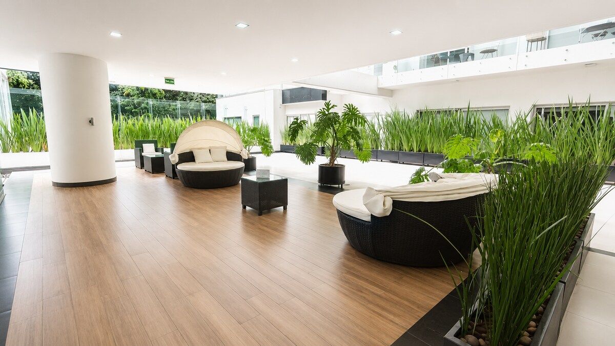 A modern lobby with a wooden floor, seating areas, and indoor plants.