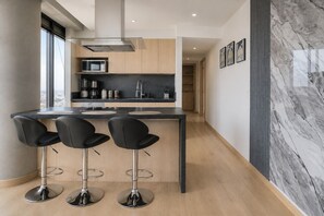 A modern kitchen with a central island, bar stools, and a view of the city. - Panoramic City View Condo on Reforma with Pool/Gym (Mexico City)