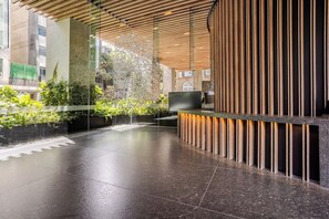 A modern reception area with a glass partition, a flat-screen TV, and a reception desk with vertical wooden slats. - Panoramic City View Condo on Reforma with Pool/Gym (Mexico City)