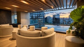 A modern lounge with a city view, featuring a large window, a wooden ceiling, and a large plant. - Panoramic City View Condo on Reforma with Pool/Gym (Mexico City)