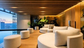 A modern lounge area with a pool, wooden flooring, and white furniture. - Panoramic City View Condo on Reforma with Pool/Gym (Mexico City)