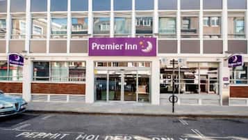 A hotel entrance with a sign for Premier Inn, a parking area marked for permit holders, and a clear view of the building's facade.